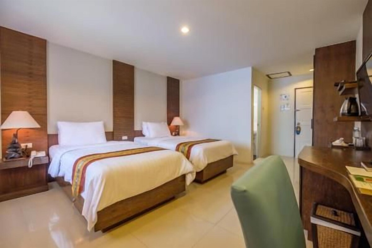 A hotel room with two beds, a desk, a chair, and a bathroom.