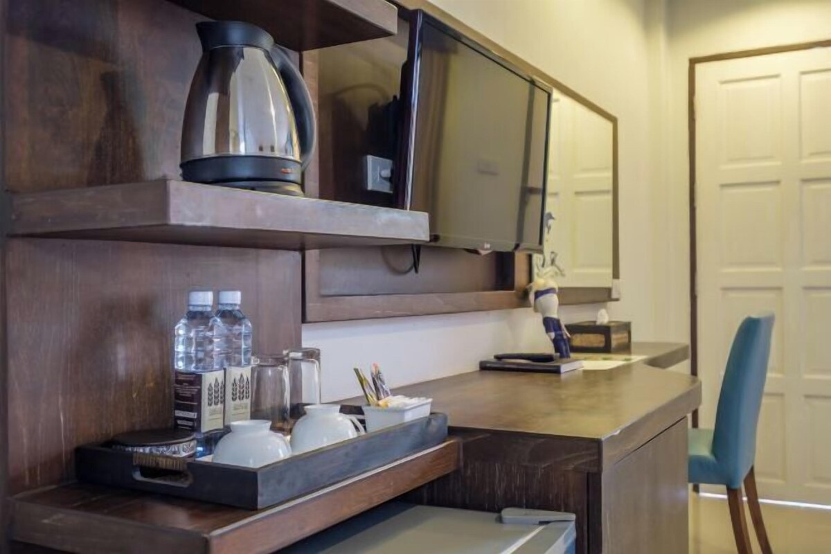 A hotel room with a wooden desk, a flat-screen TV, a coffee maker, and a tray with bottles and cups.