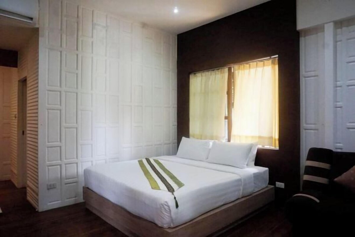 A bedroom with a bed, a window with curtains, a chair, and a door.
