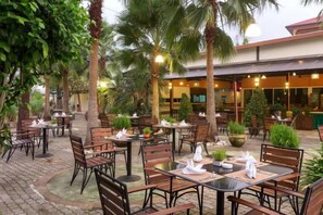 Un'area pranzo all'aperto con tavoli e sedie, circondata da palme e piante in vaso.