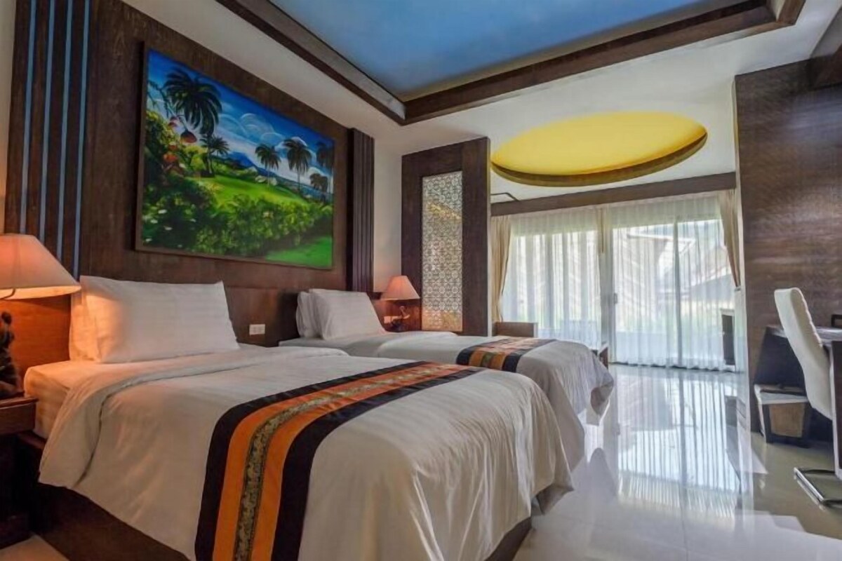 A hotel room with two beds, a painting on the wall, a desk, and a large window with curtains.