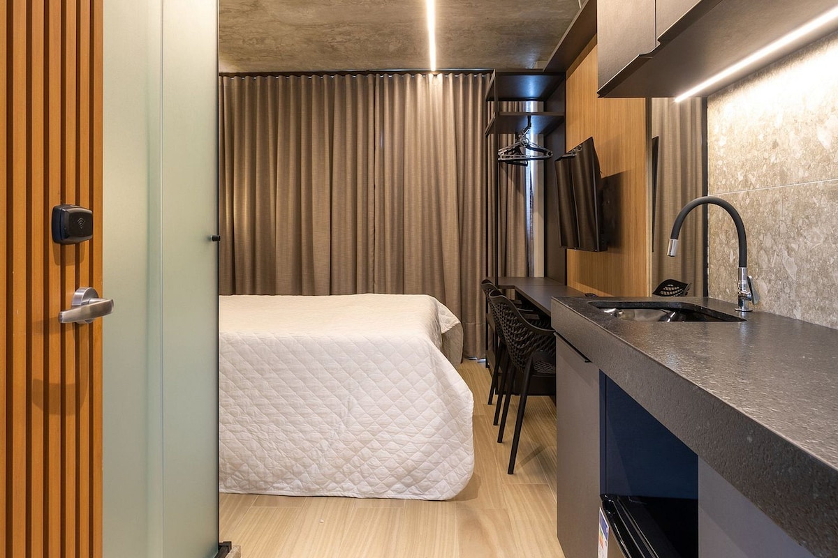 Une chambre d’hôtel compacte comprenant un coin cuisine, un lit, un espace salon et une porte en bois.