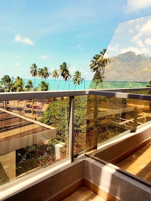 Un balcon avec vue sur une plage, des palmiers et une chaîne de montagnes.