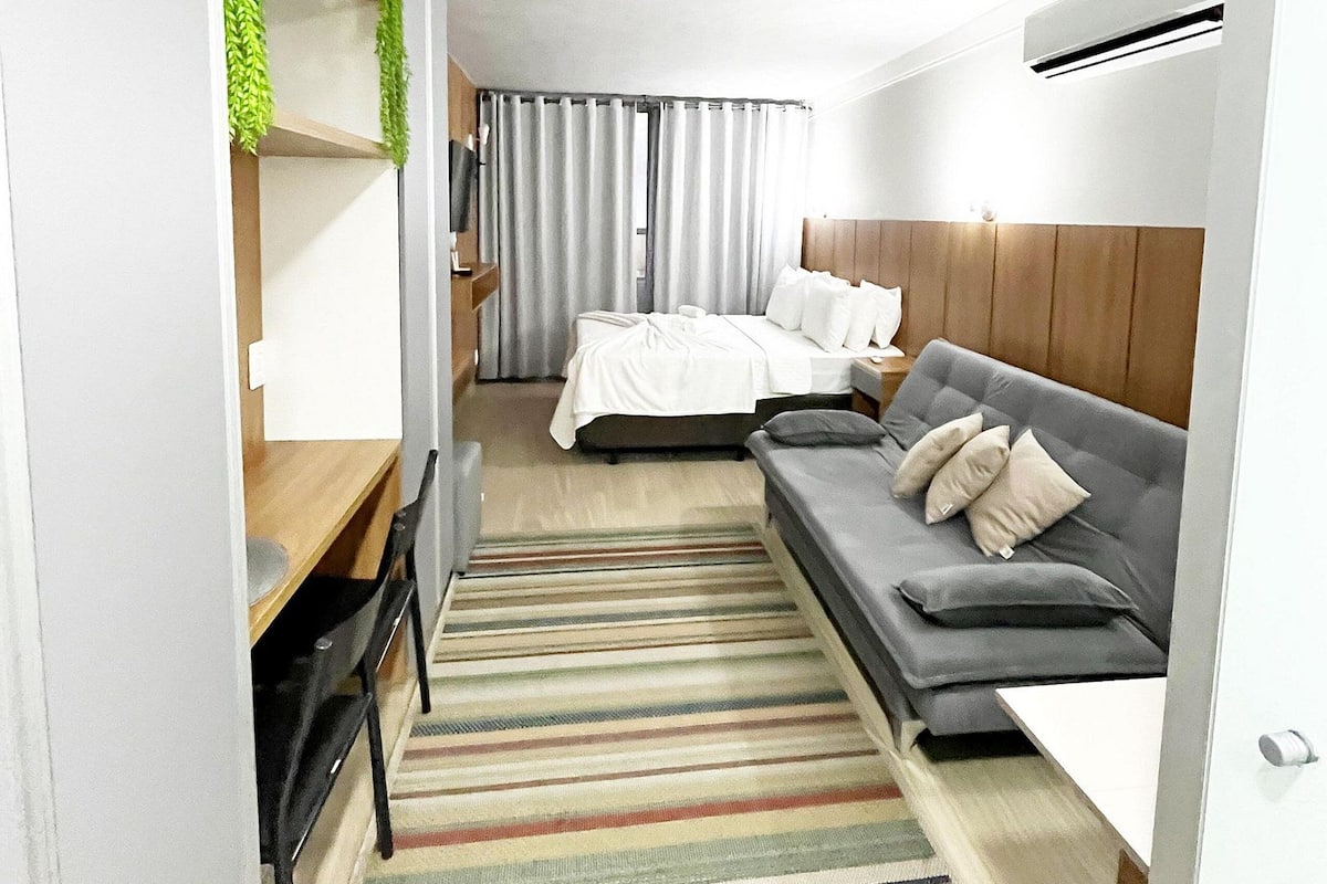 A compact hotel room with a bed, a sofa, a desk, and a chair.