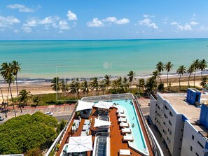 Le pont d’un navire de croisière est équipé d’une piscine, de chaises longues et offre une vue sur l’océan et la plage.