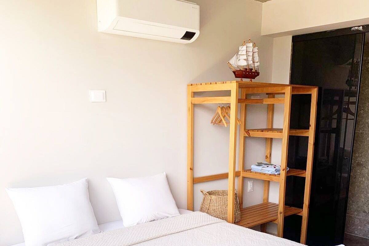 A bedroom with a large bed, a wooden wardrobe, and an air conditioning unit on the wall.