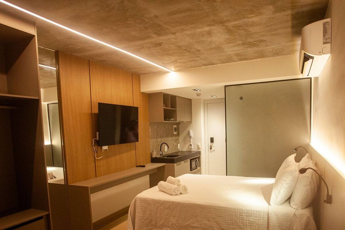 A modern hotel room with a bed, a TV, a kitchenette, and a walk-in closet.