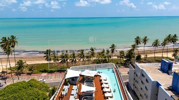 Cubierta de crucero con piscina, sillas de descanso y vistas al océano y la playa.