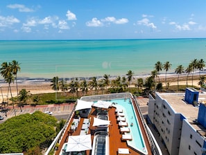 Le pont d’un navire de croisière est équipé d’une piscine, de chaises longues et offre une vue sur l’océan et la plage.