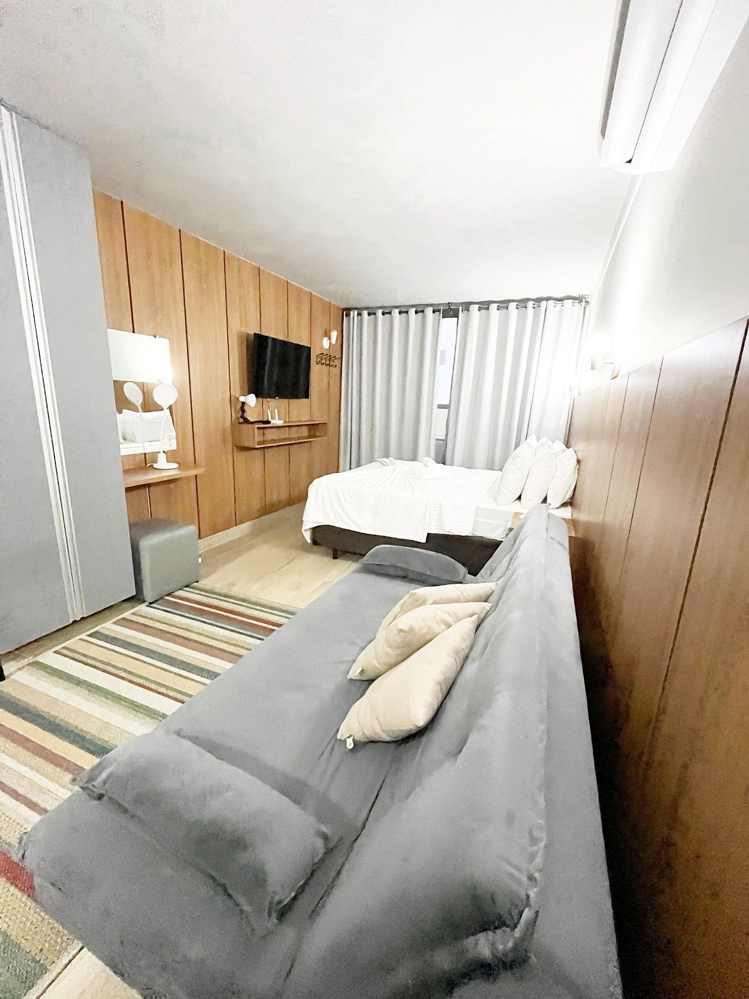 Una habitación de hotel con cama, televisión, espejo y una mesita.