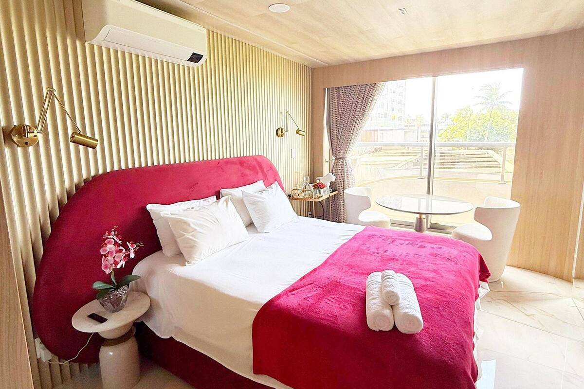 A hotel room with a large bed, a bedside table, a small table with chairs, and a window with curtains.