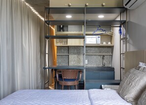Une chambre d’hôtel de taille réduite, comprenant un lit, un petit bureau, une chaise et une kitchenette.