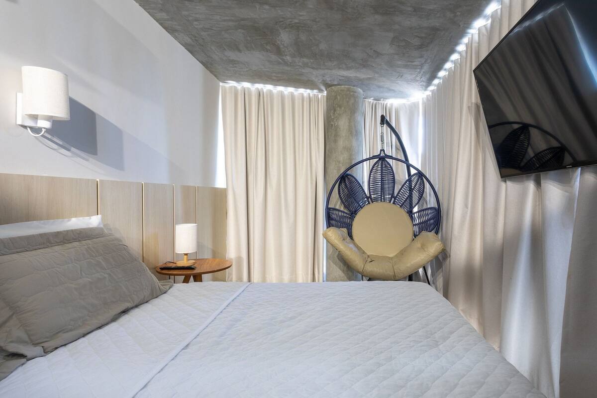 A hotel room with a bed, a chair, a TV, and curtains.