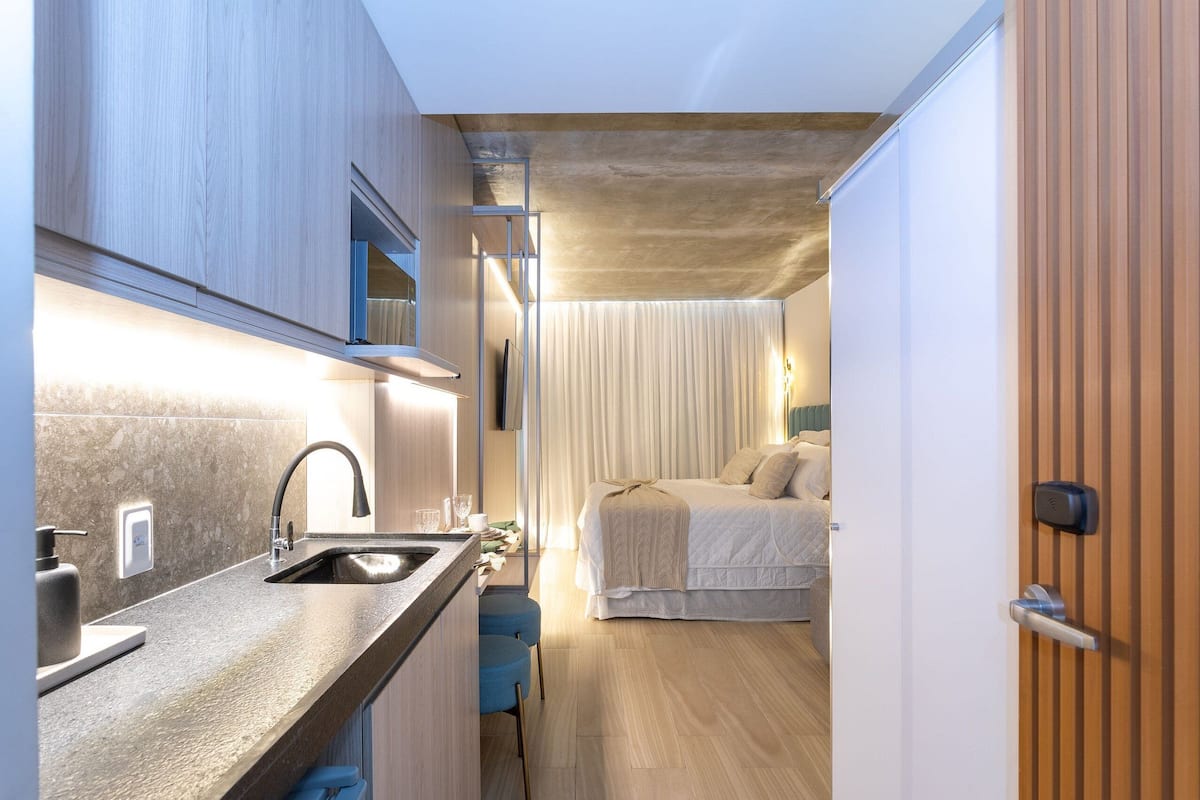 A compact room with a kitchenette, a bed, and a door.