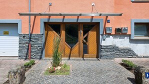 Un edificio con fachada de piedra, una entrada con puerta doble de madera y un camino de acceso pavimentado.