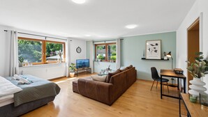 Una habitación moderna y bien iluminada con una cama, un sofá marrón, un televisor y una zona de comedor con mesa y sillas.