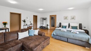 Un dormitorio moderno con un sofá de cuero marrón, una cama con edredón gris y suelo de madera.