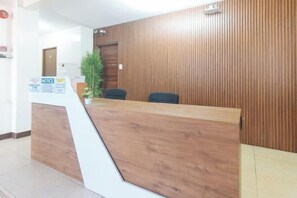 Ein Empfangsschalter mit Holzoptik, ein Blumentopf und eine Pinnwand.