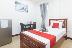 Ein Hotelzimmer mit Bett, Schreibtisch, Stuhl, Kühlschrank und einem Bild an der Wand.