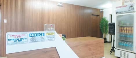 A reception desk with a wooden finish, a refrigerator with beverages, and a notice board.