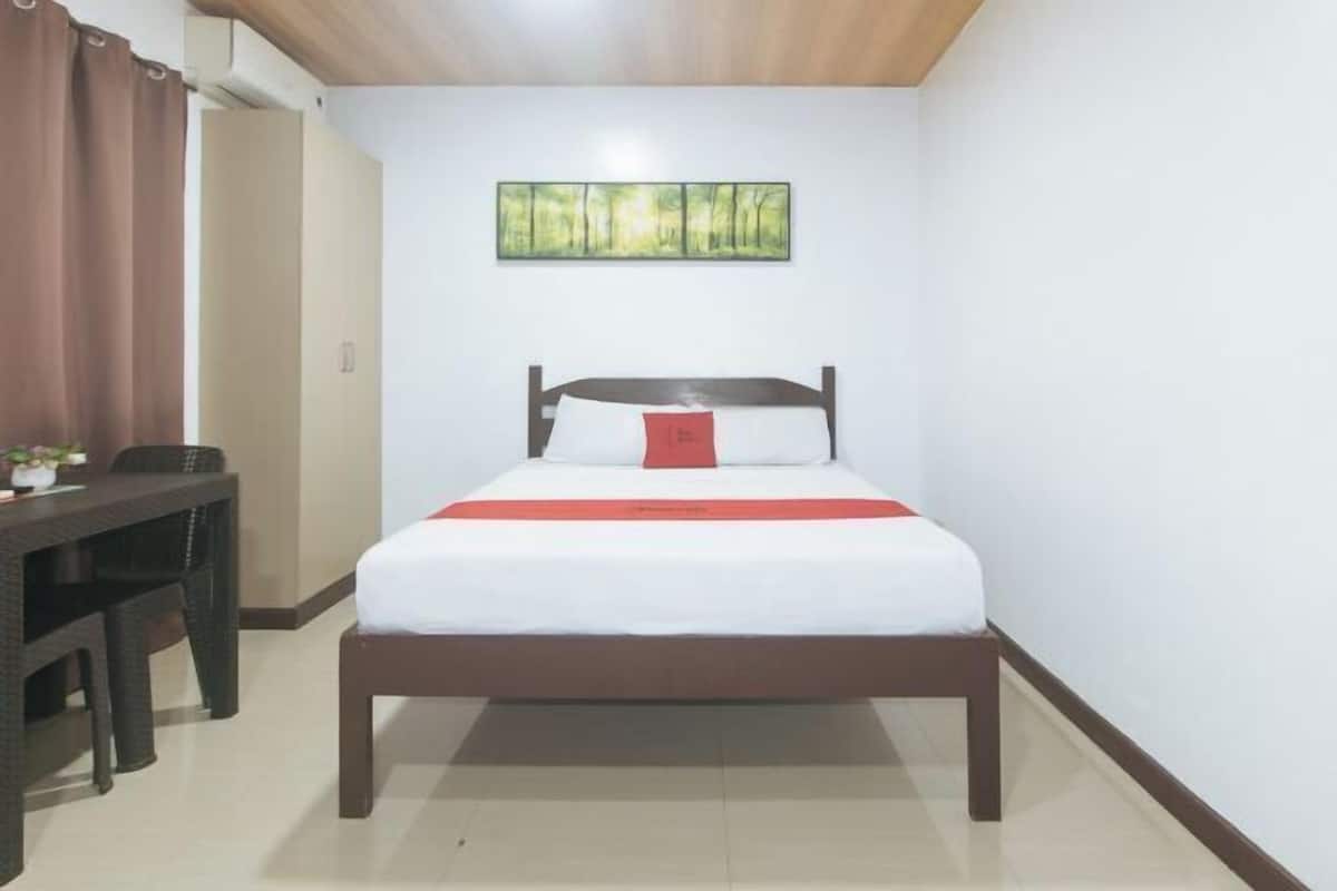 A bedroom with a bed, a nightstand, a chair, and a painting on the wall.