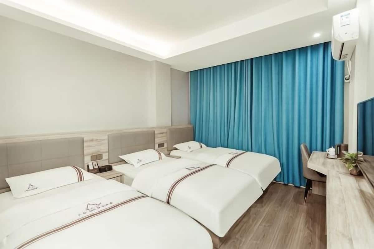 A hotel room with three beds, a desk, and a blue curtain.