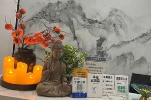 Una estatua de una figura sentada, un jarrón con bayas rojas y un candelabro con velas encendidas. Hay carteles informativos y un código QR sobre la mesa.