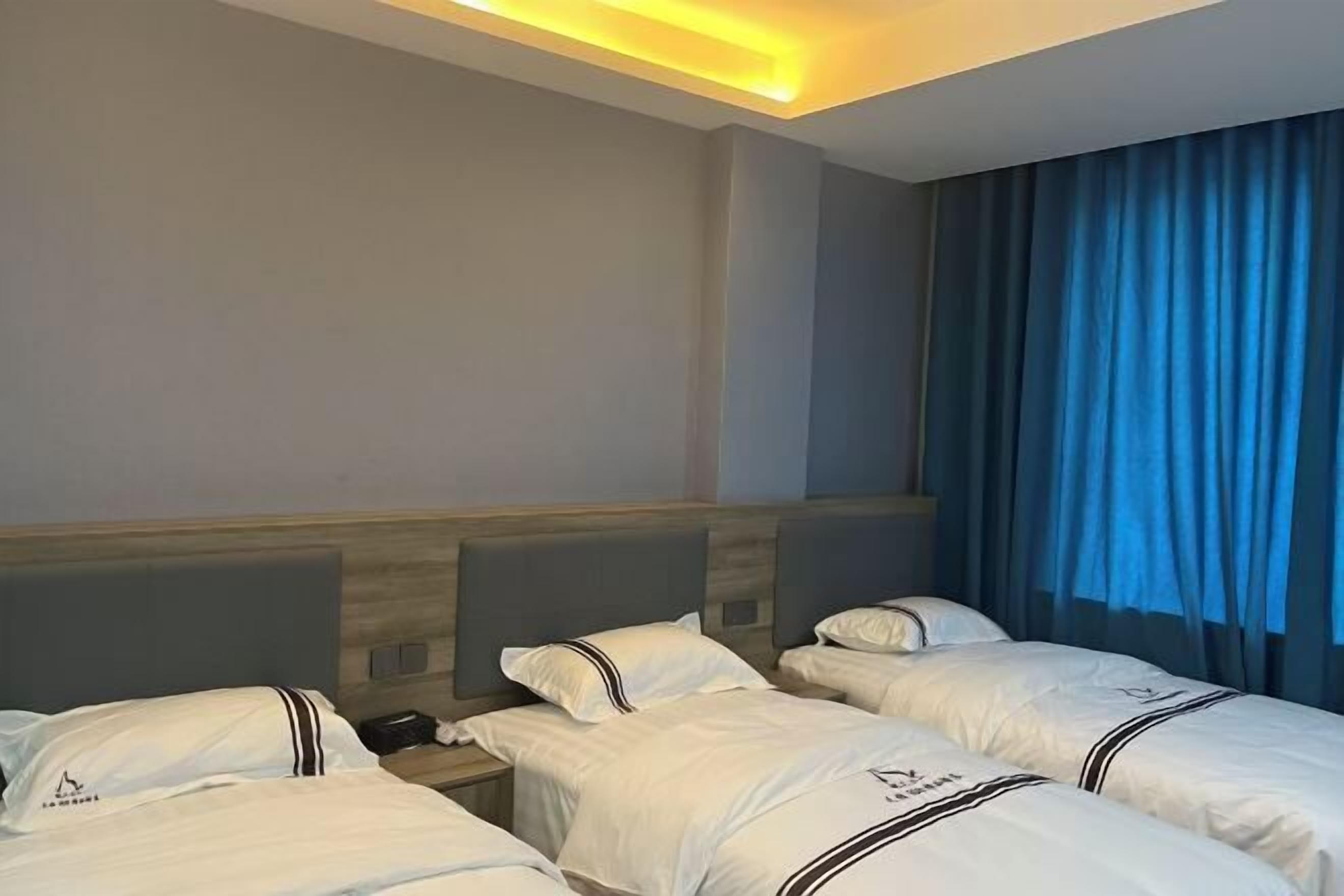 A hotel room with three beds, a wooden headboard, a nightstand, and a blue curtain.