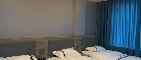 A hotel room with three beds, a wooden headboard, a nightstand, and a blue curtain.