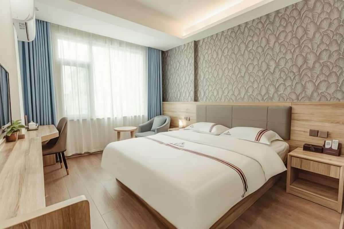 A hotel room with a large bed, a desk, a chair, a nightstand, and a window with curtains.