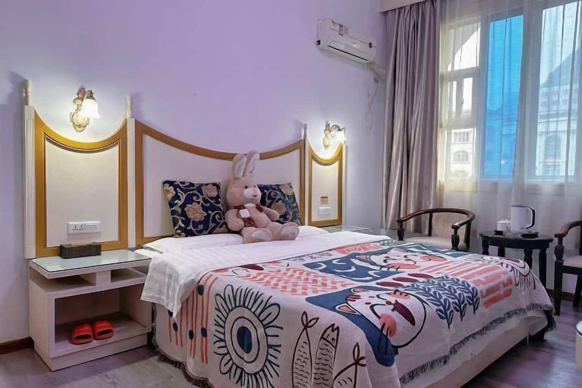 Un dormitorio con cama, mesitas de noche, una silla, un ventanal y un equipo de aire acondicionado.
