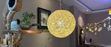A room with a hanging spherical light fixture, wooden shelves with plants, and a dining area with chairs.