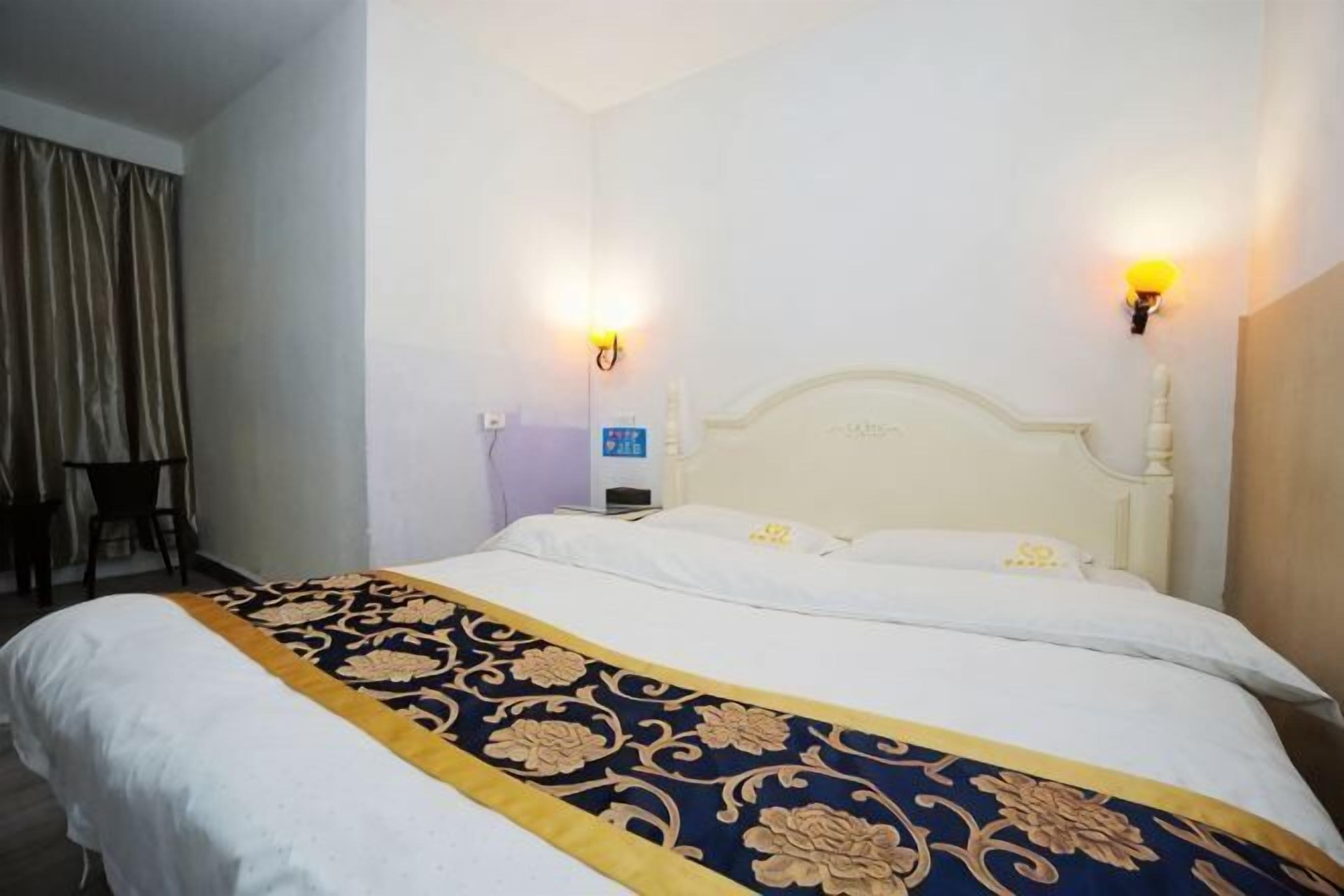 Una camera d'albergo con un letto grande, due lampade a parete, un tavolino e una tenda.
