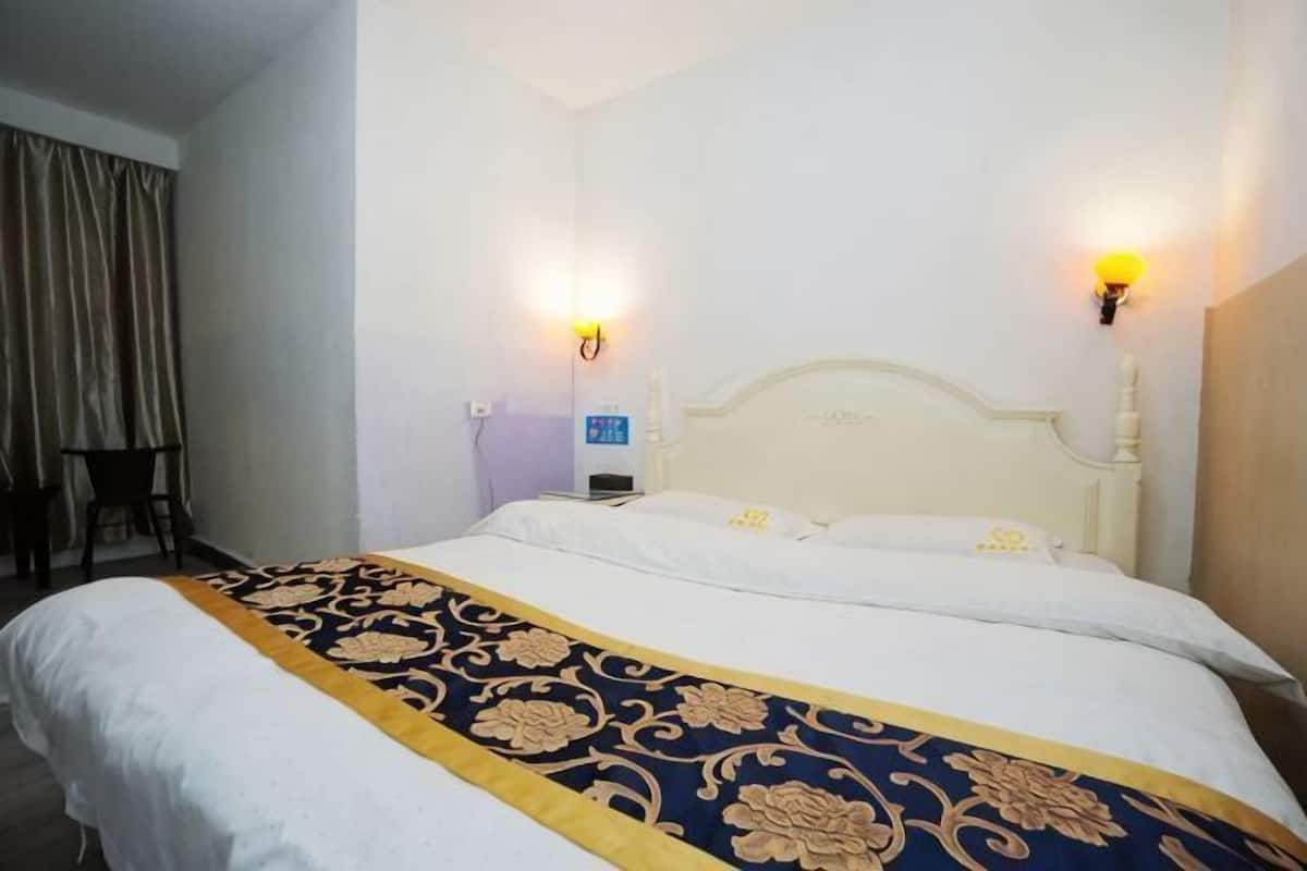 Una habitación de hotel con una cama grande, dos lámparas de pared, una mesita y una cortina.