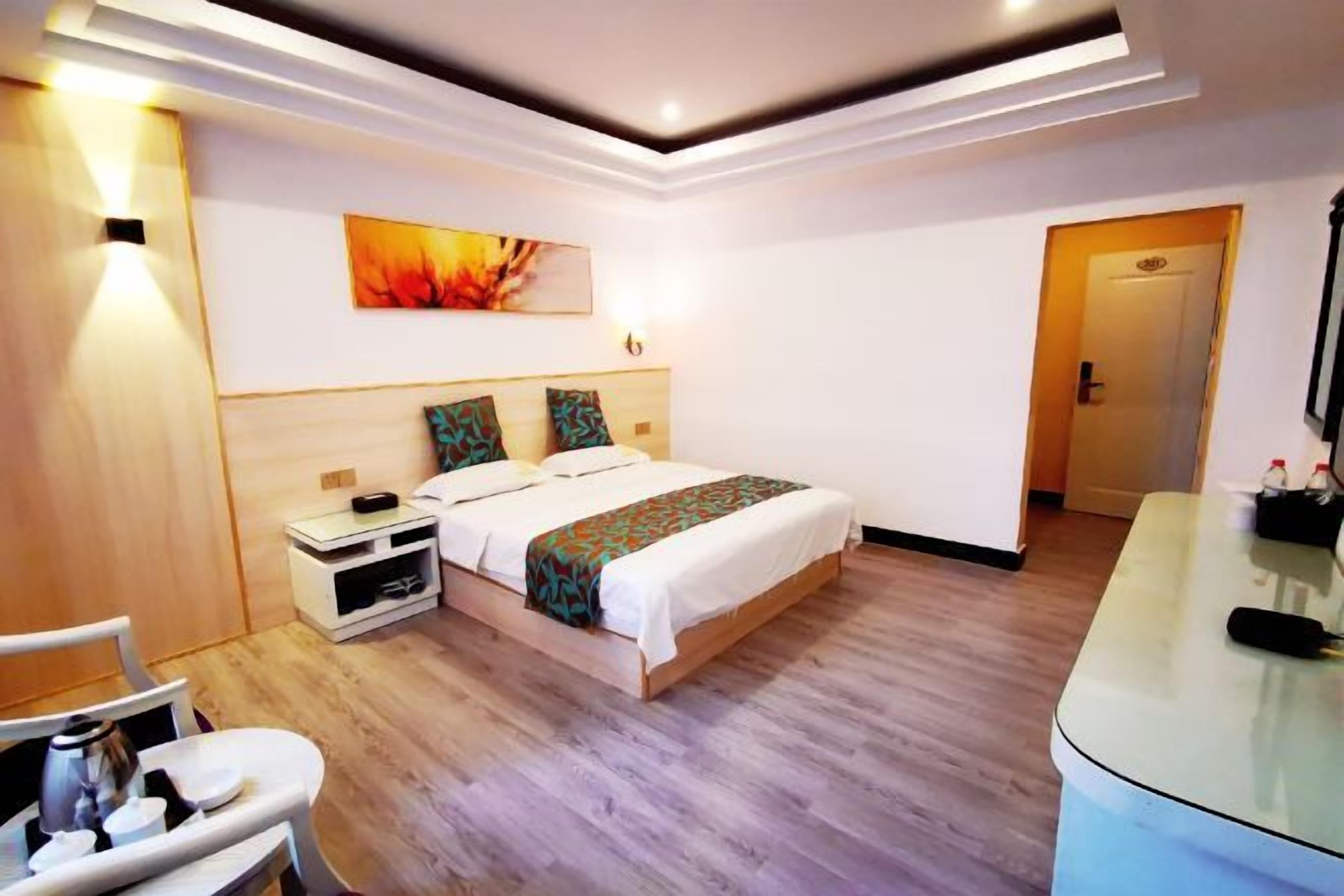 Een moderne hotelkamer met een houten vloer, een bed met beddengoed met een patroon, een nachtkastje met een lamp en een schilderij aan de muur.