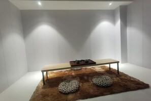 A modern interior with a minimalist design, featuring a table with a gas burner, two patterned cushions, and a fur rug.