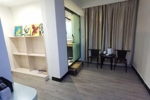 A hotel room with a wooden floor, a desk with a chair, a small table with a chair, a shelf with artwork, and a sliding door leading to a bathroom. - Jiahao Meisu Hotel (Guilin Jinshan Square) (Guilin)