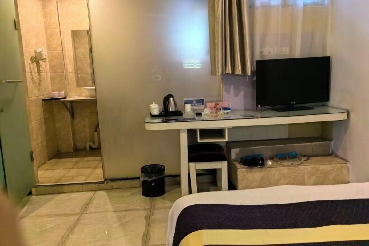 A hotel room with a bed, a desk with a television, a small table with toiletries, and a shower area.