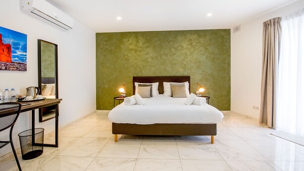 Une chambre d’hôtel avec un grand lit, un bureau avec une chaise, un tableau au mur et un mur d’accent de couleur verte.