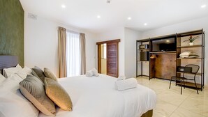 A hotel room with a large bed, a wardrobe, a desk, and a television. - Deluxe Double Room with side sea view - South Wind Guesthouse (Marsaxlokk)