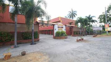 Entrada de hotel con un cartel, palmeras y una zona pavimentada.
