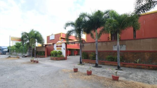 A hotel with a red and yellow facade, palm trees, and potted plants in the courtyard. - Golden Success Hotel I by RedDoorz (Paniqui)