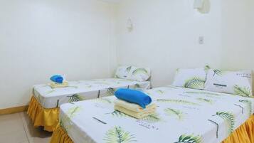 Una habitación con dos camas, cada una con una base cubierta de amarillo y una colcha con motivos botánicos.