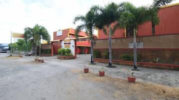 Fachada roja de un hotel, palmeras y un camino pavimentado.