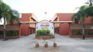 The entrance to the Golden Success Hotel with a sign, palm trees, and potted plants. - Golden Success Hotel I by RedDoorz (Paniqui)