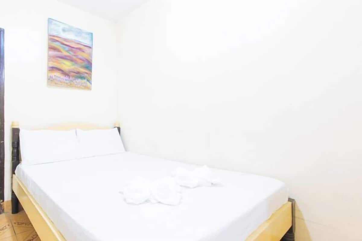 A neatly made bed with white linens and a colorful abstract painting on the wall.
