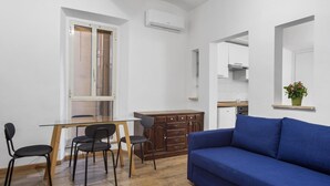 A compact living space with a dining area, kitchenette, and a blue sofa. - Colosseum Street Haven (ROMA)