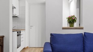A modern living room with a blue sofa, a wooden floor, a white door, and a kitchen visible through an open doorway. - Colosseum Street Haven (ROMA)