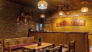 A restaurant interior with wooden furniture, a bamboo wall, and hanging lights. - The Goat Boutique Resort (Tay Hoa Lu)