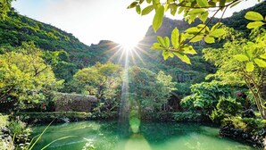 A serene natural landscape with a clear water body surrounded by lush greenery and a mountain backdrop. - The Goat Boutique Resort (Tay Hoa Lu)